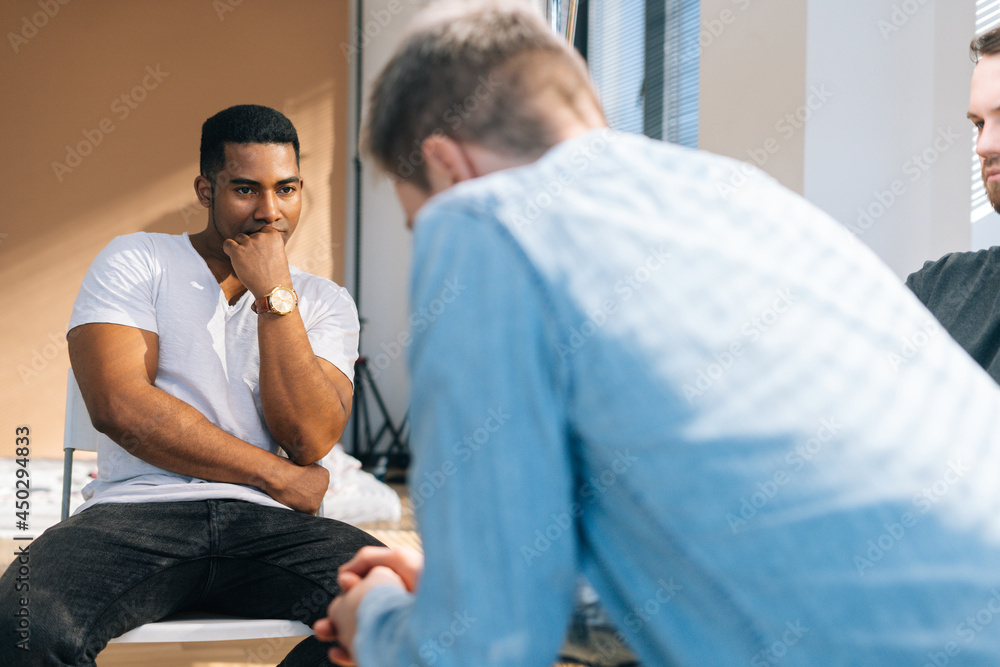 Close-up back view of depressed young man sharing mental problem sitting in circle to other patients during group therapy session. Concept of group consulting of mental health problem. Close-up back view of depressed young man sharing mental problem sitting in circle to other patients during group therapy session. Concept of group consulting of mental health problem.