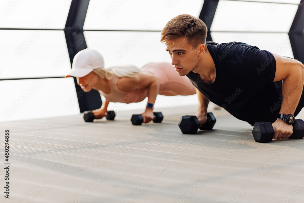 couple exercising outdoors, sportive woman and handsome muscular man are exercising on the bridge on the coast, Doing plank on kettlebell couple exercising outdoors, sportive woman and handsome muscular man are exercising on the bridge on the coast, Doing plank on kettlebell