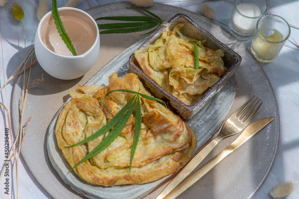 Homemade sweet frying roti (Cannabis Pancake) with Cannabis served with Cannabis tea on ceramic plate. Concept of food with cannabis herb, Treatment of medical marijuana for use in food.