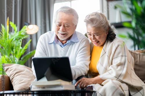 old asian senior couple retired age sitting on sofa couch video call to their family with tablet device social connect home isolation stay home state order concept,happiness senior laugh smile joyful photo