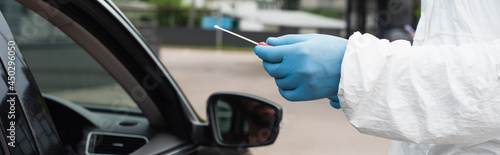 Cropped view of medical worker in hazmat suit holding pcr test near auto, banner