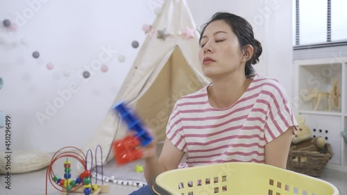 tired asian mom is breathing a sigh and mopping the sweat from her forehead while putting the toy blocks into the basket in the children’s game room.