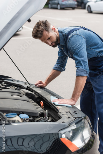 Mechanic holding rag and cleaning car with open hood outdoors