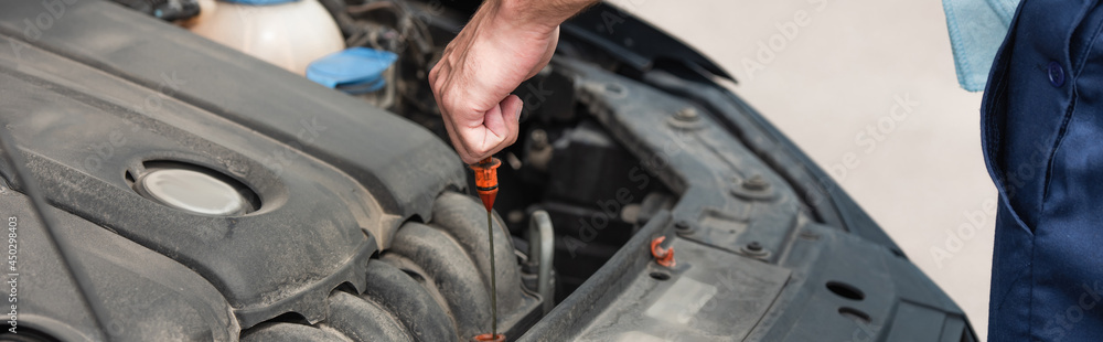 Fototapeta premium Cropped view of mechanic with dipstick checking motor oil, banner