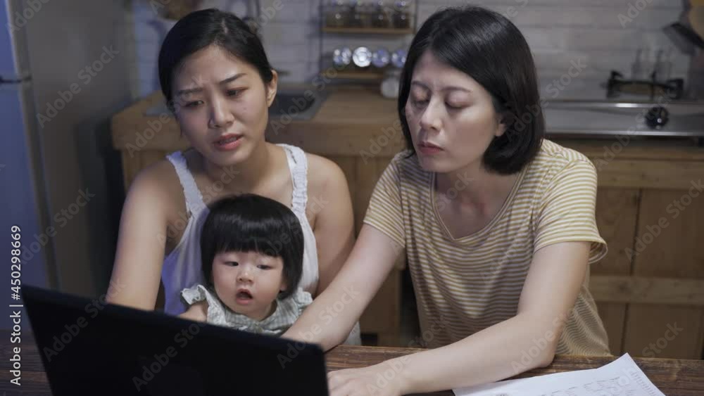 asian lgbtq family with their adopted daughter are having discussion while using laptop to make tax payment online in the dining room at night. asian lgbtq family with their adopted daughter are having discussion while using laptop to make tax payment online in the dining room at night.