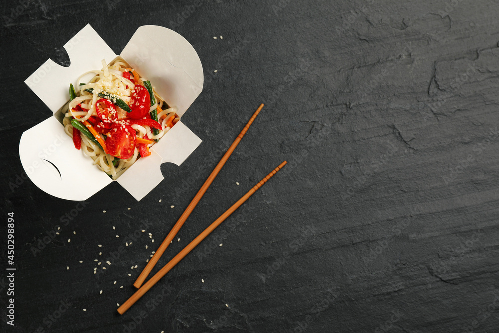 Box of vegetarian wok noodles with chopsticks on slate table, flat lay. Space for text Box of vegetarian wok noodles with chopsticks on slate table, flat lay. Space for text