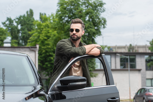 Bearded man in sunglasses standing near car with open door