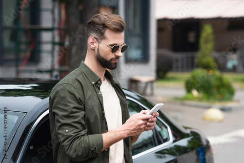 Man in sunglasses using mobile phone near car outdoors © LIGHTFIELD STUDIOS