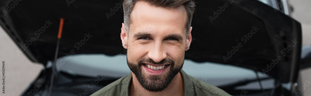 Smiling man looking at camera near blurred car, banner Smiling man looking at camera near blurred car, banner