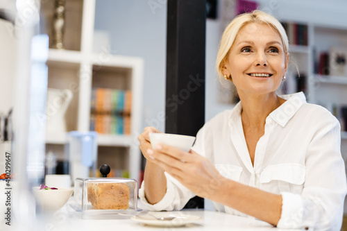White woman smiling and drinking tea while sitting in kitchen at home