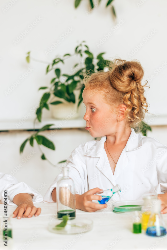 Funny little red-haired girl in white uniform doing chemical experiments in a laboratory.Back to school concept.Young scientists.Natural sciences.Preschool and school education of children. Funny little red-haired girl in white uniform doing chemical experiments in a laboratory.Back to school concept.Young scientists.Natural sciences.Preschool and school education of children.