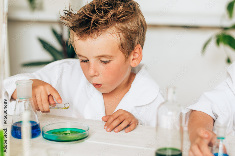 Curious little boy in white uniform conducts chemical experiments in a laboratory.Back to school concept.Young scientists.Natural sciences.Preschool and school education of children. Curious little boy in white uniform conducts chemical experiments in a laboratory.Back to school concept.Young scientists.Natural sciences.Preschool and school education of children.