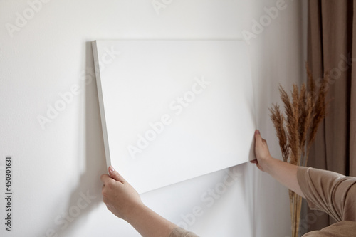 Blank canvas in female hands, picture mockup. Woman hanging canvas on white wall photo
