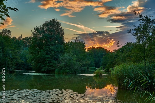 Summer Landscape.  Lake cove at dusk. Last sun rays. With lush vegetation. Water lilies,  grass and trees with reflections on the water surface. Beauty colorful sky. Dubnica, Slovakia. photo