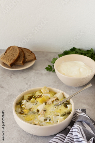 Chicken breast and sorrel soup with potatoes and sour cream, a bowl of soup on the table, bread and parsley