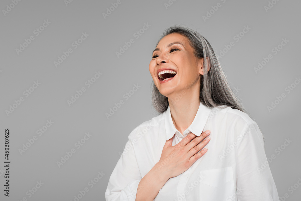 overjoyed woman with grey hair touching chest while laughing isolated on grey overjoyed woman with grey hair touching chest while laughing isolated on grey
