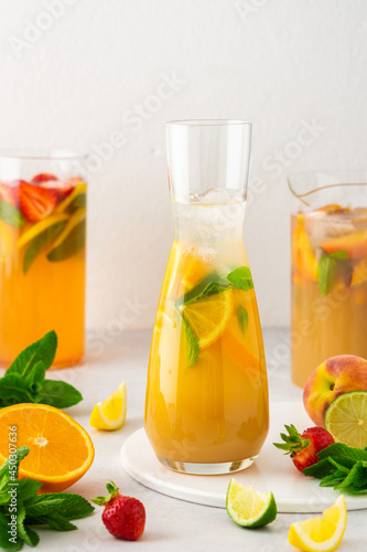 Jugs of fresh refreshing fruit drinks with fruit wedges, summer cold juices with ice