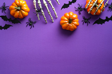 Halloween flat lay composition with pumpkins, bony hands, spiders, bats on purple background. Happy halloween banner mockup.