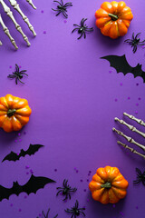 Happy Halloween poster mockup. Flat lay bony hands, pumpkins, bats silhouettes on purple background. Top view with copy space.
