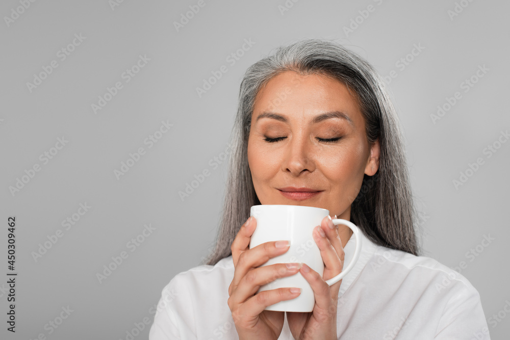pleased middle aged woman enjoying flavor of tea isolated on grey pleased middle aged woman enjoying flavor of tea isolated on grey