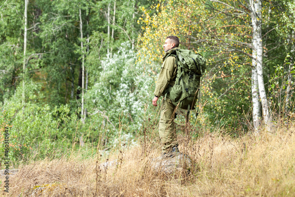 Young man travelling alone with a backpack. Concept of active tourism, camping in the forecast, trekking and hiking during vacations. Green background. Copy space for text Young man travelling alone with a backpack. Concept of active tourism, camping in the forecast, trekking and hiking during vacations. Green background. Copy space for text