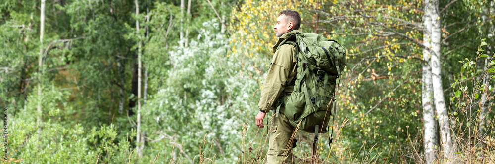 Young man travelling alone with a backpack. Concept of active tourism, camping in the forecast, trekking and hiking during vacations. Green background. Copy space for text banner Young man travelling alone with a backpack. Concept of active tourism, camping in the forecast, trekking and hiking during vacations. Green background. Copy space for text banner