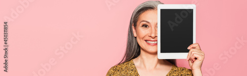 Tableau sur toile happy mature woman obscuring face with digital tablet isolated on pink, banner
