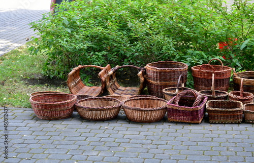 A small collection of wicker backets made by hand and used to carry various items seen on a pavement next to a massive shrub during a medieval fair on a Polish countryside photo