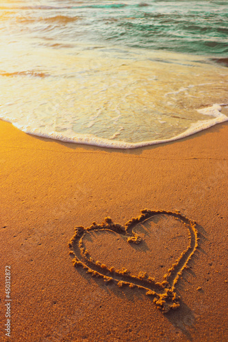 A heart drawing in the sand. Ocean waves on the beach. Happy holiday concept. Vertical background photo