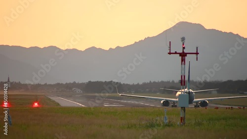 Passenger airplane taking off against colorful sunset. Ljubljana airport runway in Slovenia. Plane spotting. Large aircraft takes off. Rear view of plane ascending. Static shot, real time photo