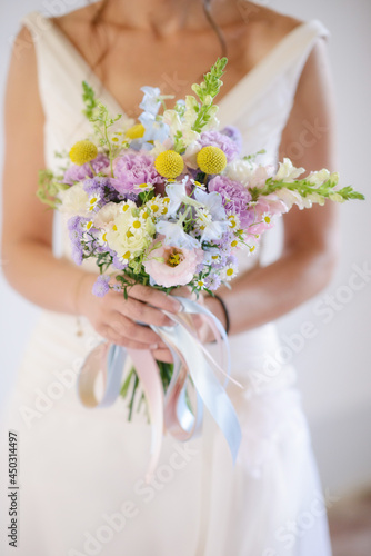 Sposa in abito bianco che regge fra le mani un bouquet di fiori di campo colorati photo