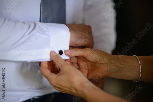 Mani femminili che sistemano il polsino con i gemelli della camicia bianca indossata dallo sposo photo