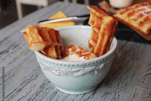 Sliced Belgian waffles with ice cream and caramel in a light blue bowl 