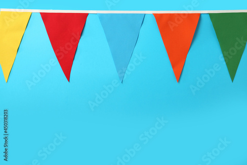 Bunting with colorful triangular flags on light blue background. Space for text