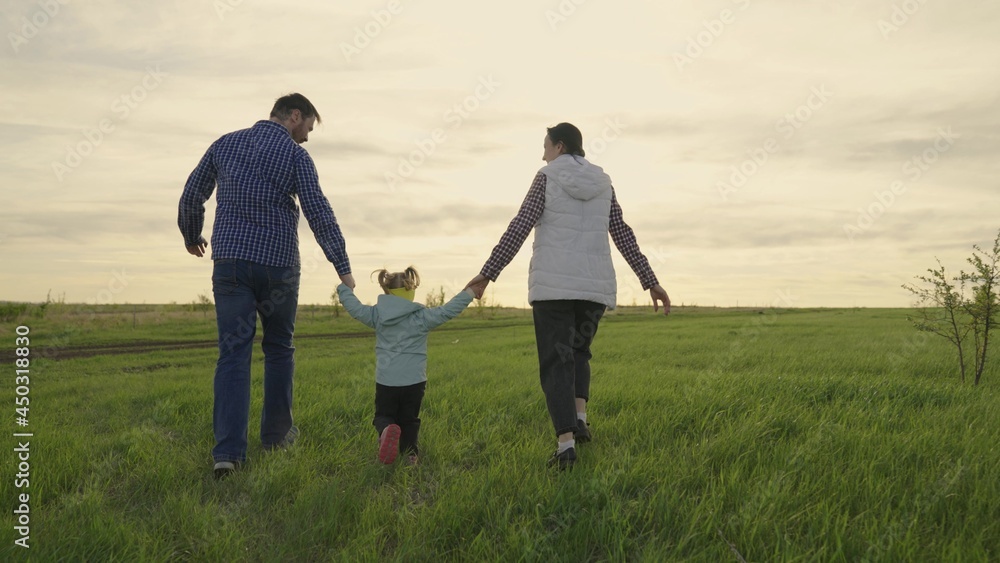 Mom, dad are a child, a daughter is running on the green grass, playing on the field. Happy family walks in the park holding hands in the summer at sunset. Teamwork. Happy healthy childhood