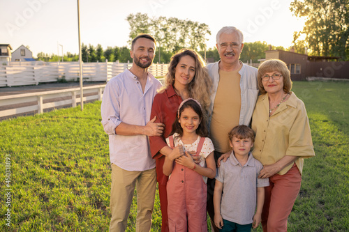 Large family of three generations standing on green lawn in the countryside