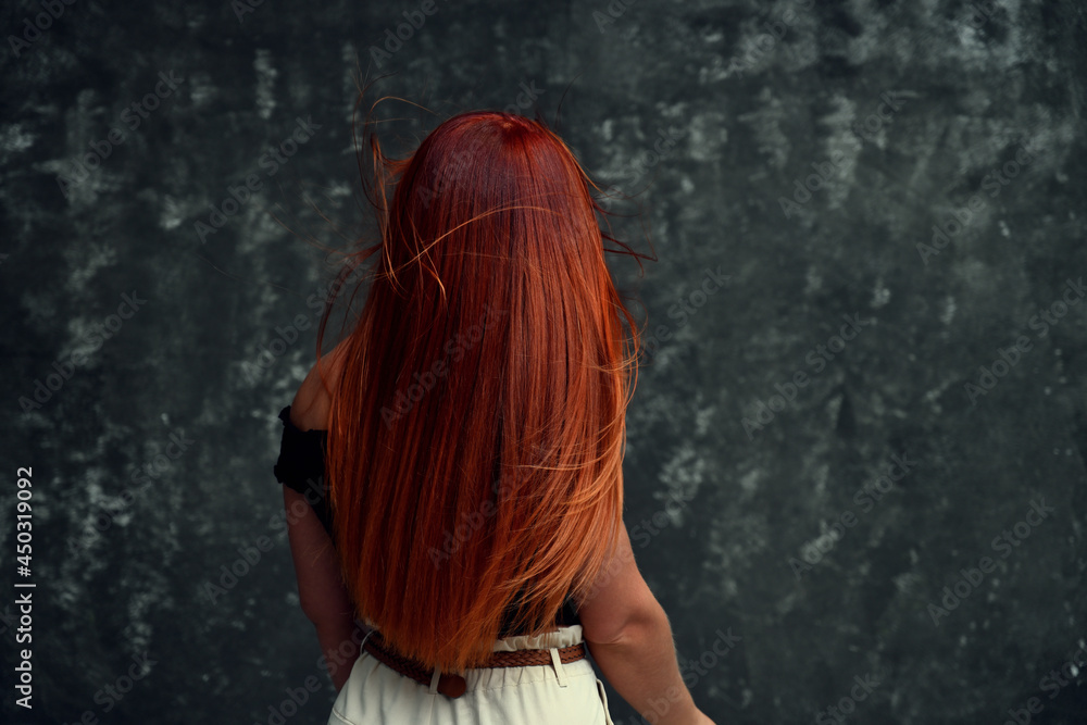 portrait of a young girl from behind in the studio. redhead caucasian model stands right on gray background portrait of a young girl from behind in the studio. redhead caucasian model stands right on gray background