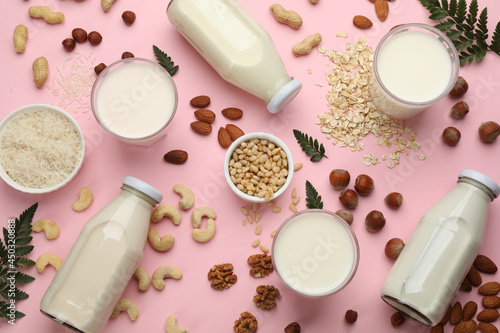 Different vegan milks and ingredients on pink background, flat lay