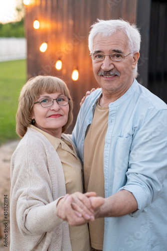 Happy senior man and woman holding by hands in front of camera outdoors