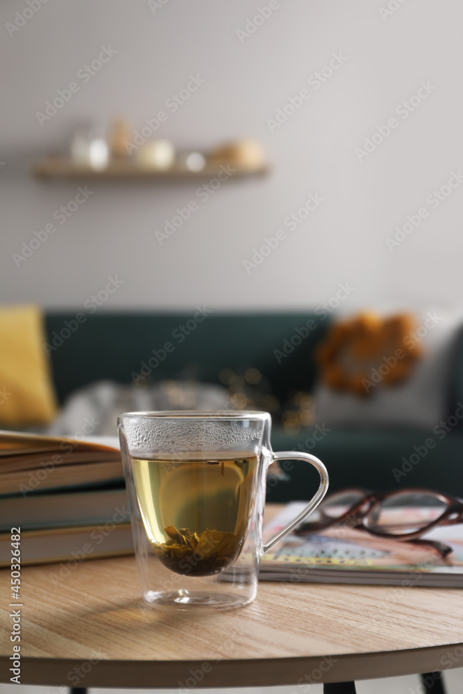 Glass cup of freshly brewed tea on wooden table in living room. Cozy home atmosphere Glass cup of freshly brewed tea on wooden table in living room. Cozy home atmosphere