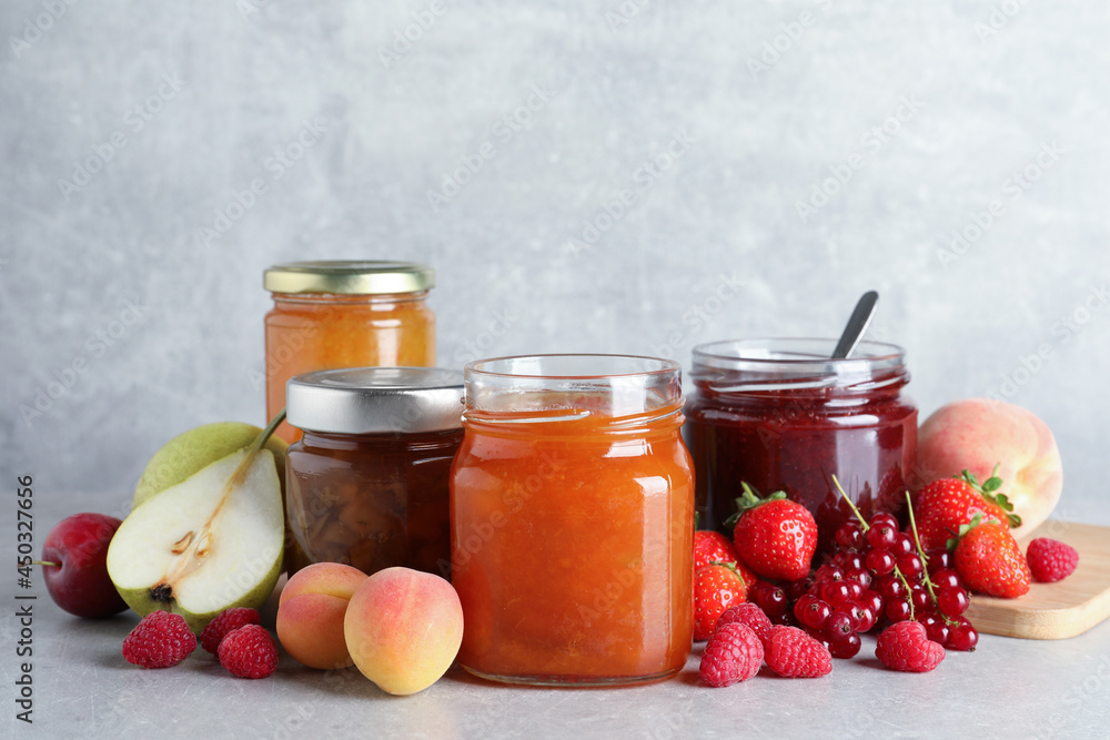 Jars with different jams and fresh fruits on grey table Jars with different jams and fresh fruits on grey table