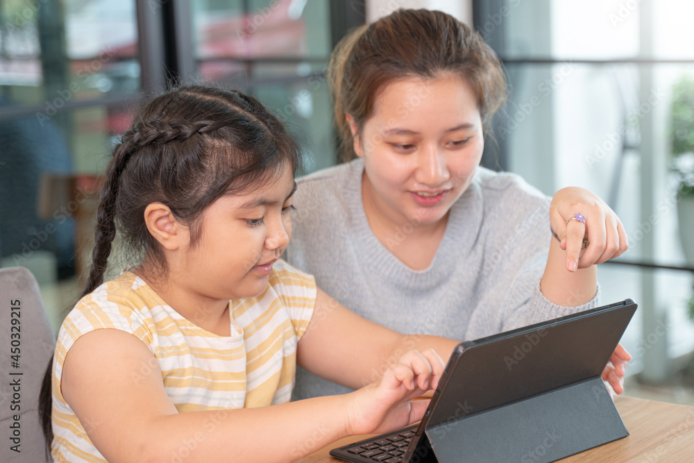 Woman helps small girl child using tablet computer to join virtual classroom for remote learning from home during Covid-19 lockdown.During the virus epidemic,Online learning,online education. Woman helps small girl child using tablet computer to join virtual classroom for remote learning from home during Covid-19 lockdown.During the virus epidemic,Online learning,online education.