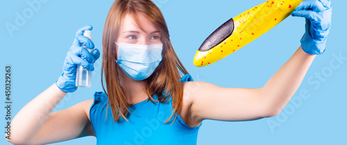 The blonde woman in blue t-shirt wearing medical face mask holding in her hands disinfectant spray to travel in pandemic.