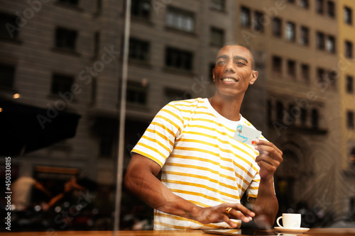 Handsome young african man in cafe drinking coffee. Portrait of happy man with credit card drinking coffee in cafe..