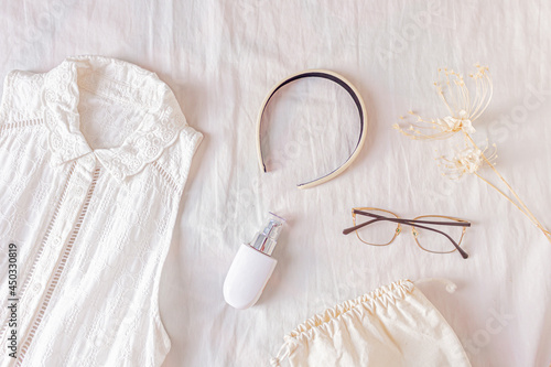 Female fashion look with stylish clothes and accessories. Lifestyle flat lay, top view. Composition with off white dress, cotton bag, headband, glasses, foundation makeup and dried flowers. 