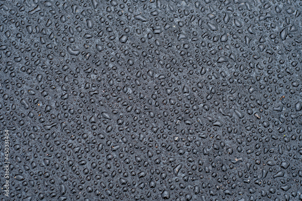 Dark background with large water droplets on newly paved asphalt. Road surface wet from rain after repair work. Dark background with large water droplets on newly paved asphalt. Road surface wet from rain after repair work.