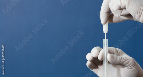 mouth swab in the hands of a doctor or nurse wearing white surgical gloves, inserted into a transporter vial, with a blue background