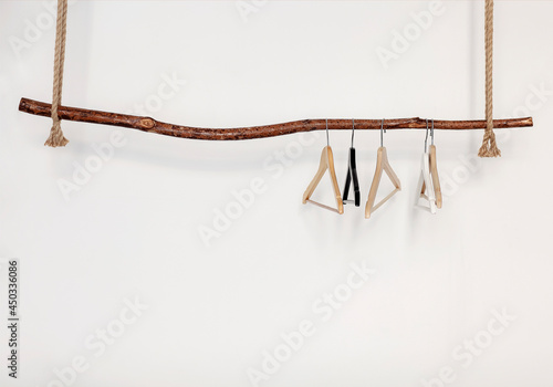 Photo Five empty clothes hangers hanging on wooden rustic style rod on thick rope, iso
