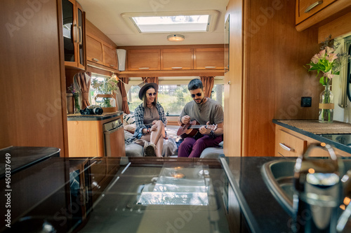 Young man playing guitar while sitting next to his girlfriend in house on wheels