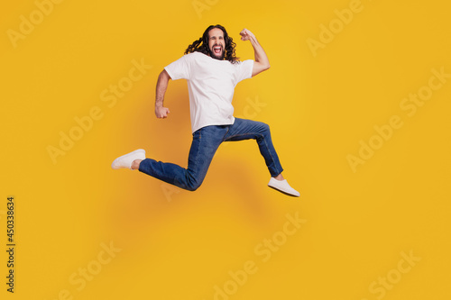 Portrait of sporty energetic guy run excited jump on yellow background